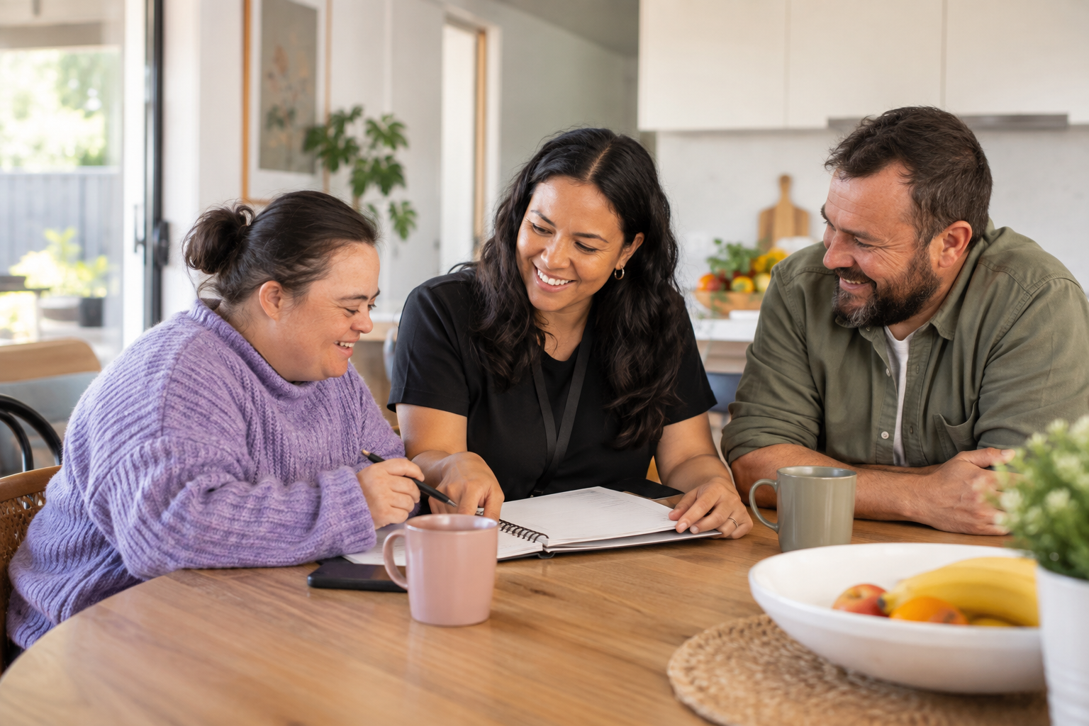 Two adults and a disability support worker planning everyday activities together at a kitchen table.